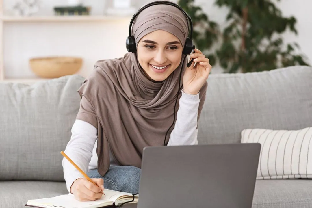 A smiling student with a headset takes notes during a live online lesson