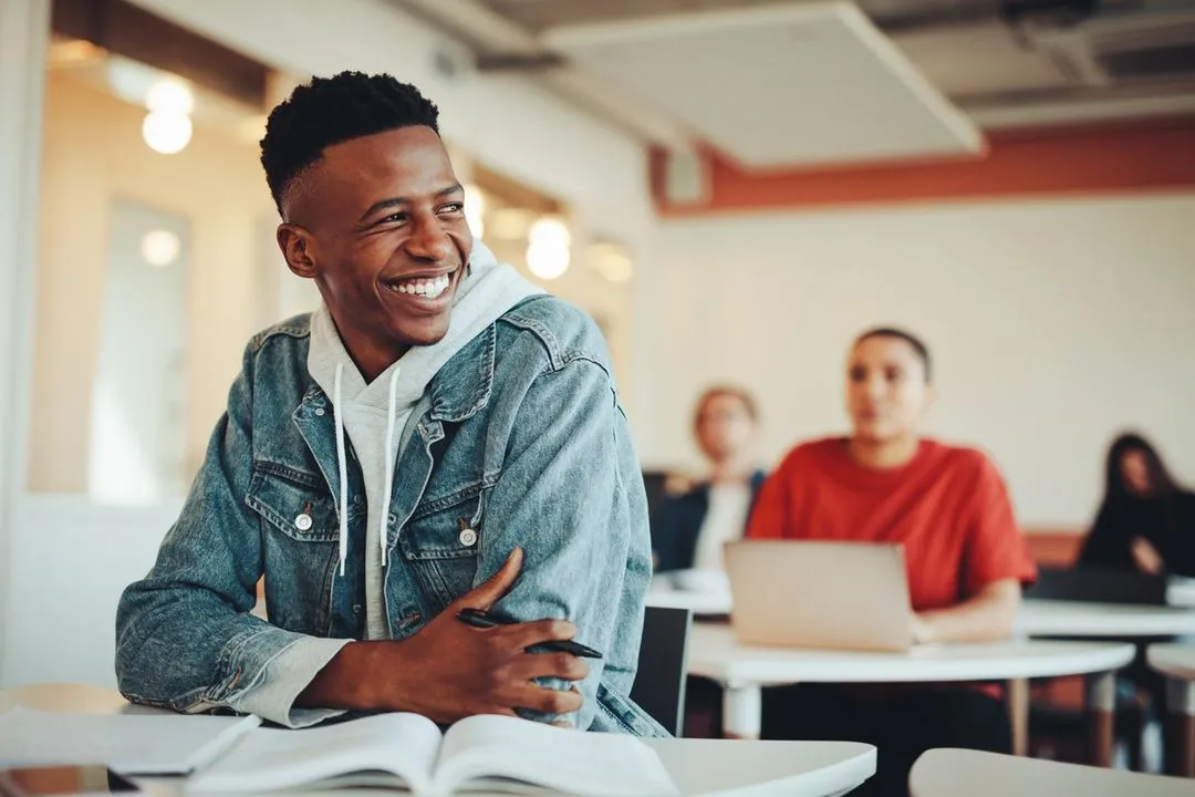 A smiling high school student working at a classroom desk