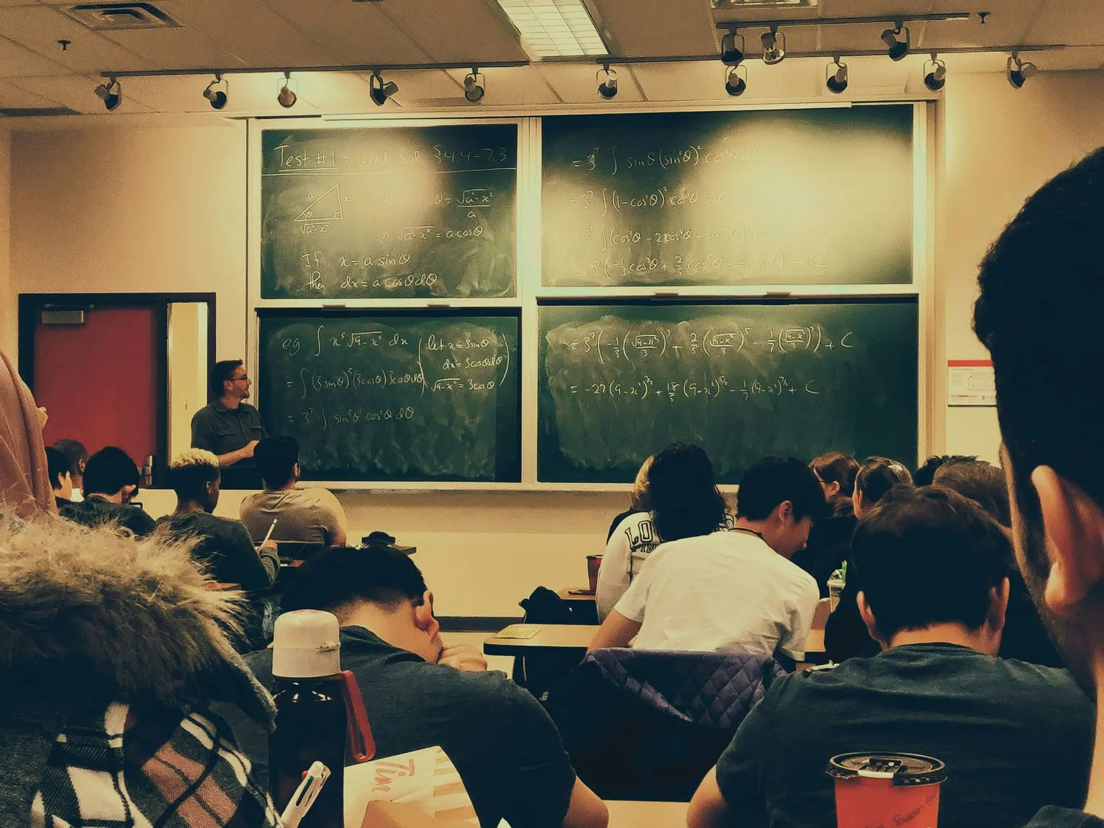 Students in a lecture hall facing a wall of chalkboards